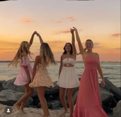 four women standing on the beach with their arms in the air and one holding her hands up