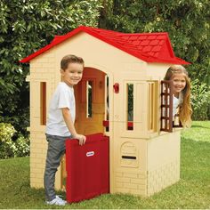 two children standing in front of a play house with a red roof and door open