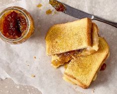 two pieces of toast with jam on the side next to a jar of jelly and a knife