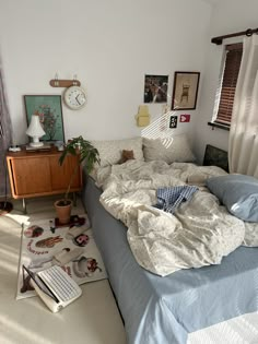 an unmade bed sitting in a bedroom next to a dresser and window with curtains