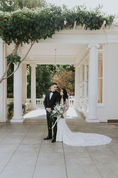 a bride and groom kissing in front of a white building with columns on either side