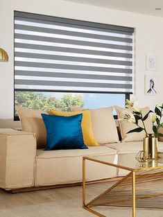 a living room filled with furniture and a large window covered in roman blind shades on the windowsill