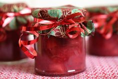 red jars with ribbons and bows in them sitting on a tablecloth covered table cloth