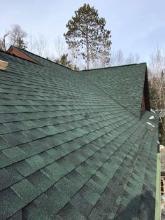 the roof of a house with green shingles and trees in the backgroud