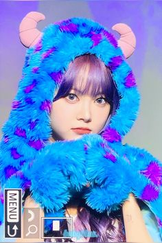 a woman with purple hair wearing a blue furry monster costume and holding her hands up to her face