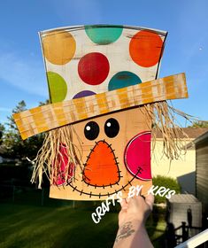 a person holding up a paper plate with a scarecrow on it's head