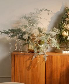 two vases with plants and ornaments on top of a wooden cabinet next to a wall