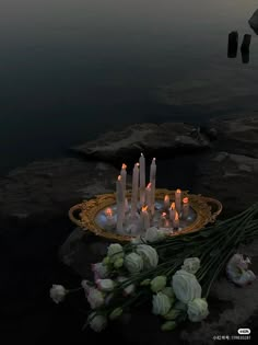 there are many candles that are on the rocks by the water with flowers in front of them