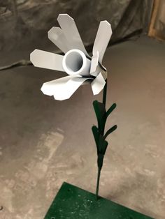 a white paper flower sitting on top of a green table next to a gray wall