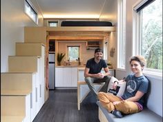 two people sitting on a bench in a tiny home with stairs leading up to the kitchen