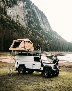 two people standing on the roof of a truck with a tent attached to it's roof