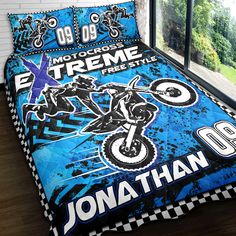 a bed covered in a blue and black cover with a dirt bike design on it