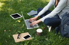 a woman sitting in the grass with her laptop and other electronic devices on her lap