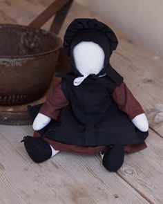 a small doll sitting on top of a wooden table next to an old frying pan