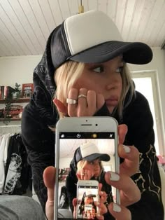 a woman taking a selfie with her cell phone while wearing a baseball cap and jacket