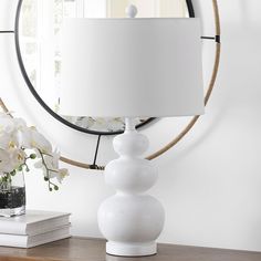 a white lamp sitting on top of a wooden table next to a mirror and flowers