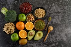 an assortment of fruits and vegetables are arranged on a black surface with spoons next to them