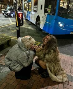 two women sitting on the ground in front of a bus talking to each other and laughing