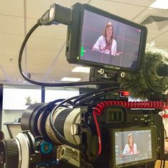 a video camera with a woman on the screen in front of it and another person sitting at a table behind it