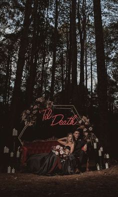 two people sitting on a red couch in the middle of a forest with candles around them