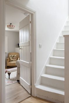 an open door leading to a living room with white walls and wood flooring on the stairs