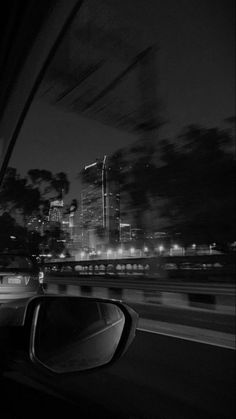 black and white photograph of city at night taken from inside a car with rear view mirror