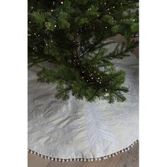 a small christmas tree is on the floor under a white blanket with fringe trimmings