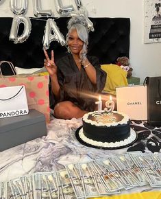 a woman sitting in front of a birthday cake with candles on it and money bags around her