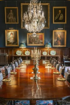 a large wooden table surrounded by chairs in a room with paintings on the wall and chandelier