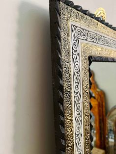 an ornate gold and black framed mirror hanging on a white wall next to vases