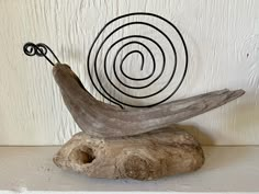 a bird sculpture sitting on top of a piece of driftwood next to a spiral design