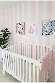 a baby's room with pink and white stripes on the walls, a crib in front of a potted plant