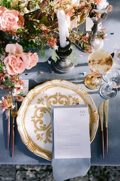 the table is set with gold and white plates, silverware, and pink flowers