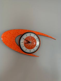 an orange and white clock is hanging on the wall in front of a gray background