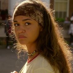 a woman with long hair wearing a bandana and looking at the camera while standing in front of a building