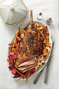 a large roast on a platter with carrots, potatoes and other food items