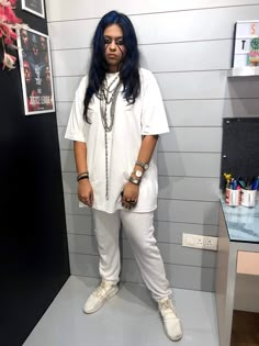 a woman with blue hair standing in front of a black and white wall wearing all white