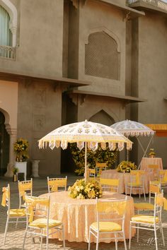 an outdoor dining area with yellow and white tables and chairs, umbrellas and flowers