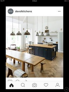 an open kitchen and dining room area with wooden table, benches, pendant lights hanging from the ceiling