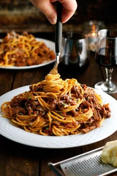 someone is eating spaghetti with meat and sauce on a plate next to some wine glasses