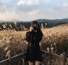 a woman taking a photo with her camera in front of a field full of tall grass