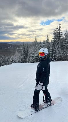 a snowboarder is standing on the top of a snowy hill with trees in the background