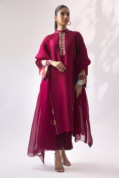 A berry rawsilk kurta with floral appliqué work placed on the sleeve cuffs is a bright summer outfit choice. It is paired with tonal rawsilk culottes and an organza dupatta, embellished with colorful appliqué flowers around the edges, creating a coordinated look. Cotton Silk Sharara For Spring Festive Occasions, Spring Festive Cotton Silk Sharara, Traditional Wear With Embroidered Sleeves For Eid, Cotton Silk Traditional Wear With Embroidered Sleeves For Eid, Designer Cotton Silk Palazzo Set For Spring, Spring Designer Cotton Silk Palazzo Set, Bollywood Style Anarkali Set With Embroidered Sleeves, Traditional Cotton Silk Salwar Kameez With Embroidered Sleeves, Eid Anarkali Set With Embroidered Sleeves For Designer Wear