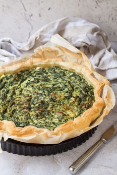 a spinach pie sitting on top of a table next to a knife and fork