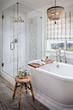 a white bath tub sitting next to a wooden stool in a bathroom under a chandelier