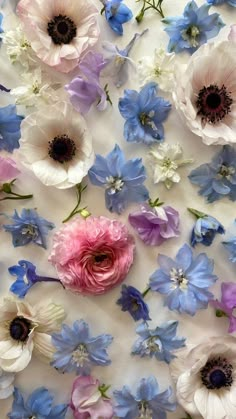 an array of flowers are arranged on a white tablecloth with blue, pink and purple flowers