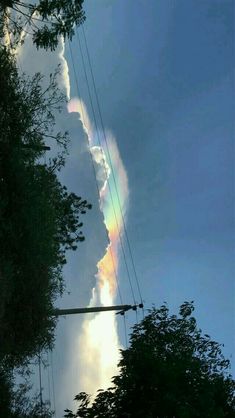 a rainbow appears in the sky as clouds loom over trees and power lines on a cloudy day