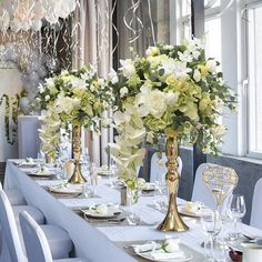 a long table with white and yellow flowers in tall gold vases on top of it