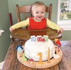 a little boy sitting in front of a cake on top of a wooden table next to a chair