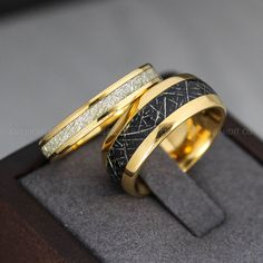 two gold rings with black and white designs on them sitting on a wooden stand in front of a gray background